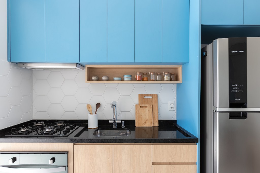 Apê de 56 m² ganha canto alemão com sapateira e bar na bancada da cozinha. Projeto de Thais Monfré, Na foto, cozinha com marcenaria azul e backsplash hexagonal.