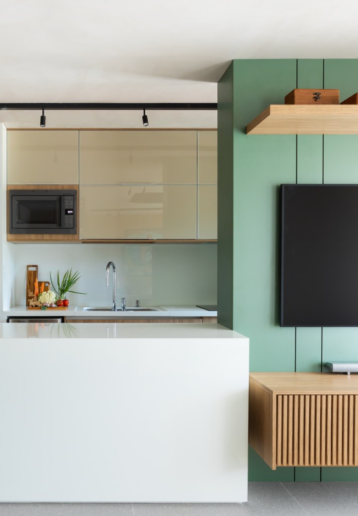 Cozinha americana; cozinha integrada com bancada branca; sala de tv com parede verde.