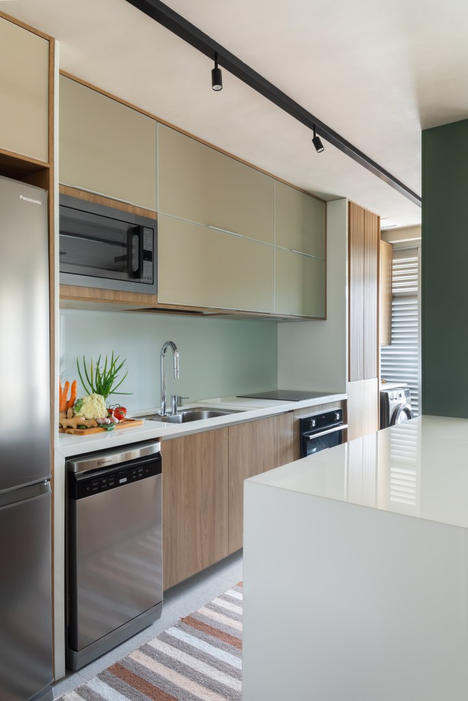 Cozinha integrada com bancada branca e marcenaria verde clara.