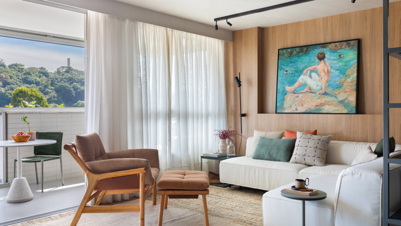 Sala de estar com sofá branco, poltrona de couro, tapete bege e iluminação com trilho de spots.