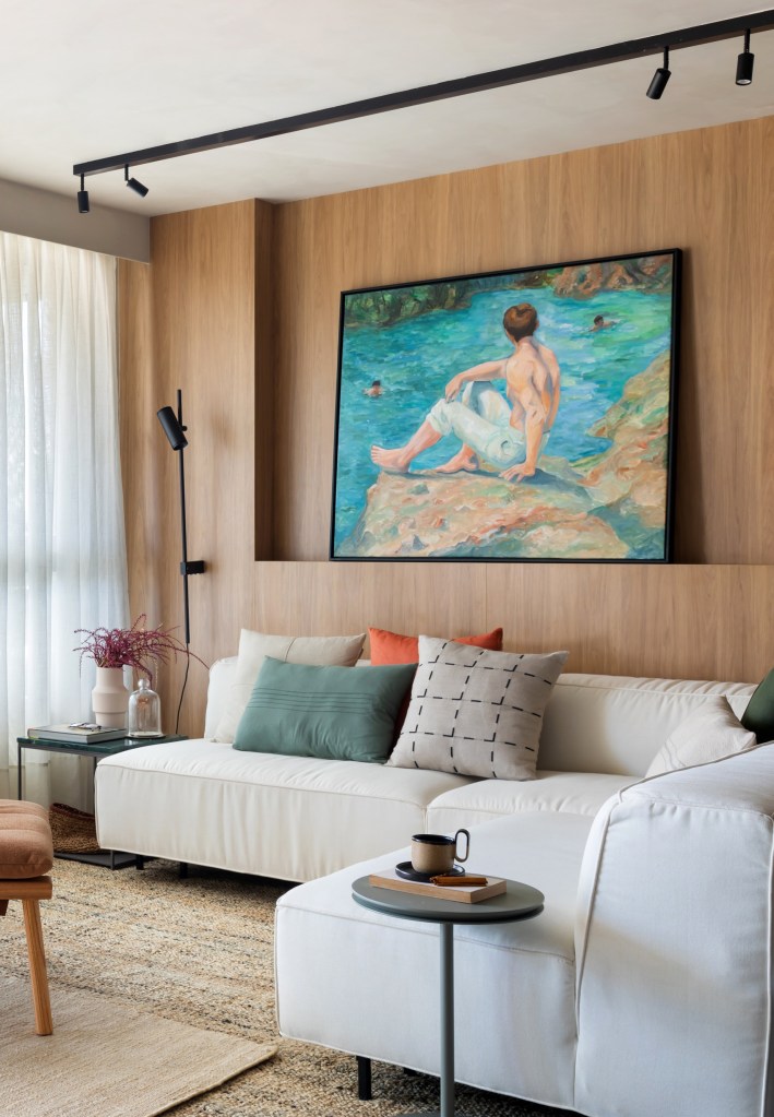 Sala de estar com tapete bege, sofá branco, parede revestida de madeira.