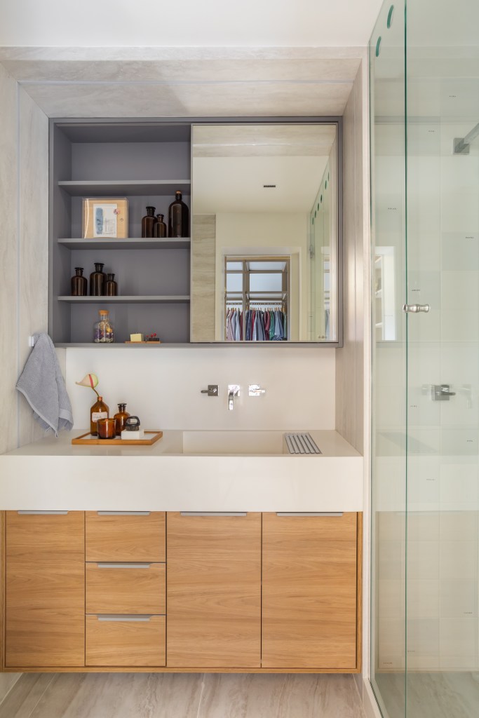 Banheiro branco com box de vidro e armário aéreo espelhado.