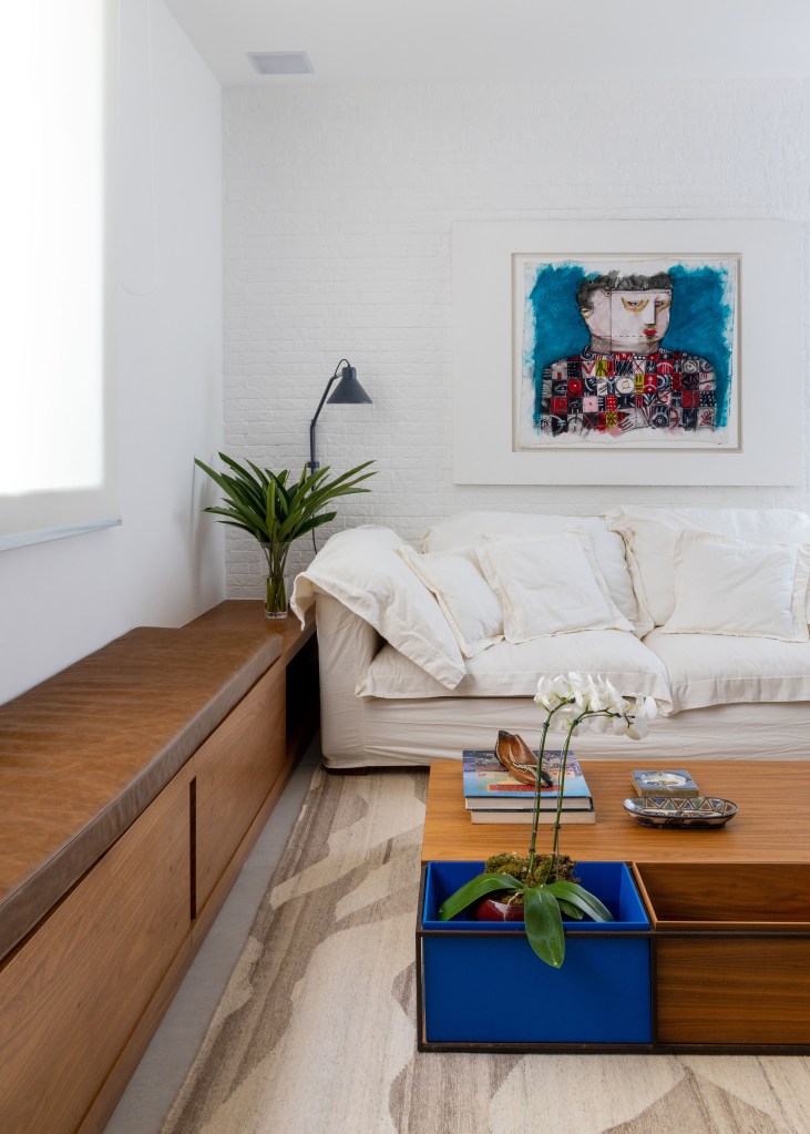 Sala de estar com sofá branco, banco de madeira e couro e mesa de centro de madeira.