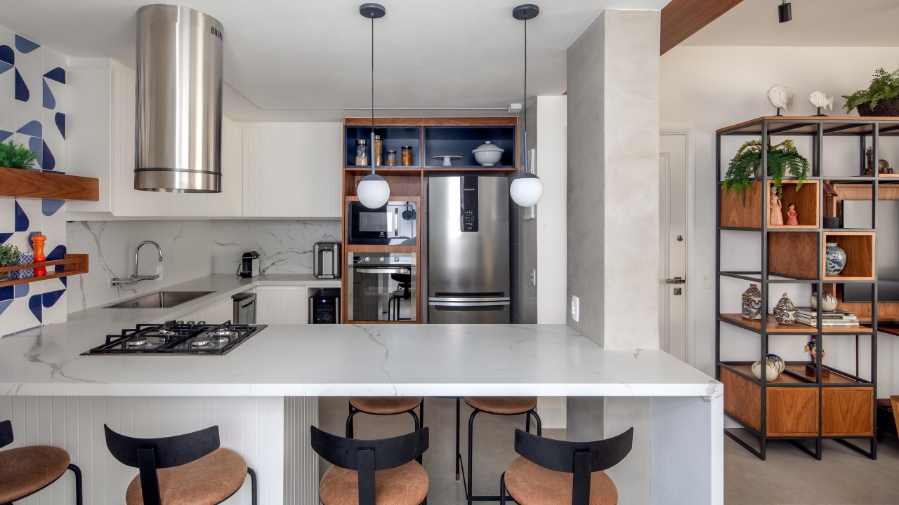 Cozinha integrada com marcenaria branca, bancada branca e parede de azulejos azuis.