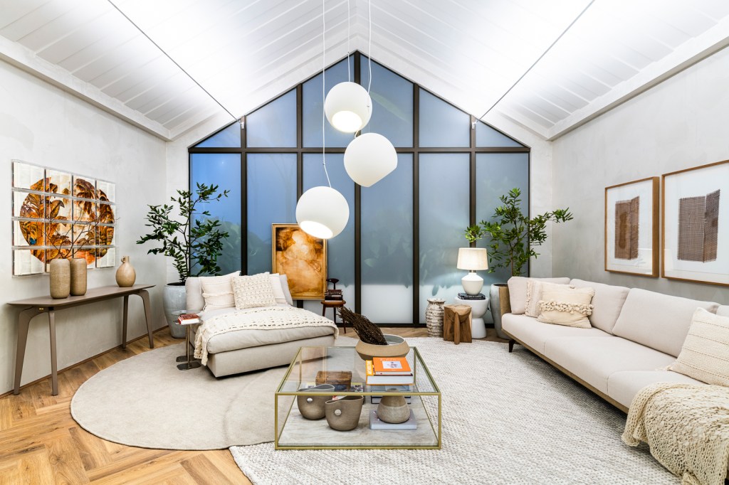 Sala de estar branca clara com tapete off white, poltrona e sofás brancos, luminárias esféricas e mesa de centro de vidro.