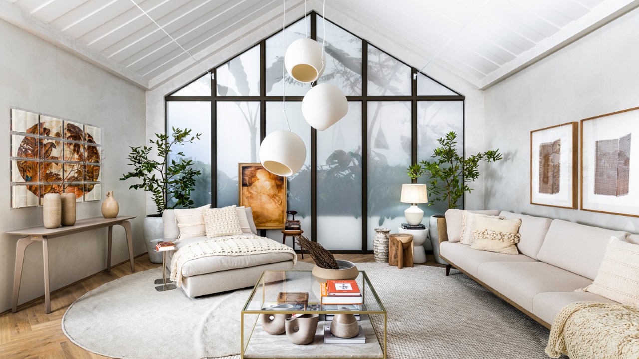 Sala de estar branca clara com tapete off white, poltrona e sofás brancos, luminárias esféricas e mesa de centro de vidro.