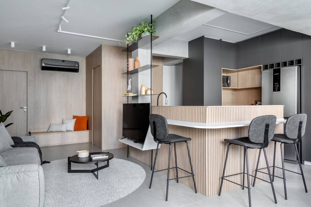 Balcão da cozinha vira painel de TV neste apê de 80 m²