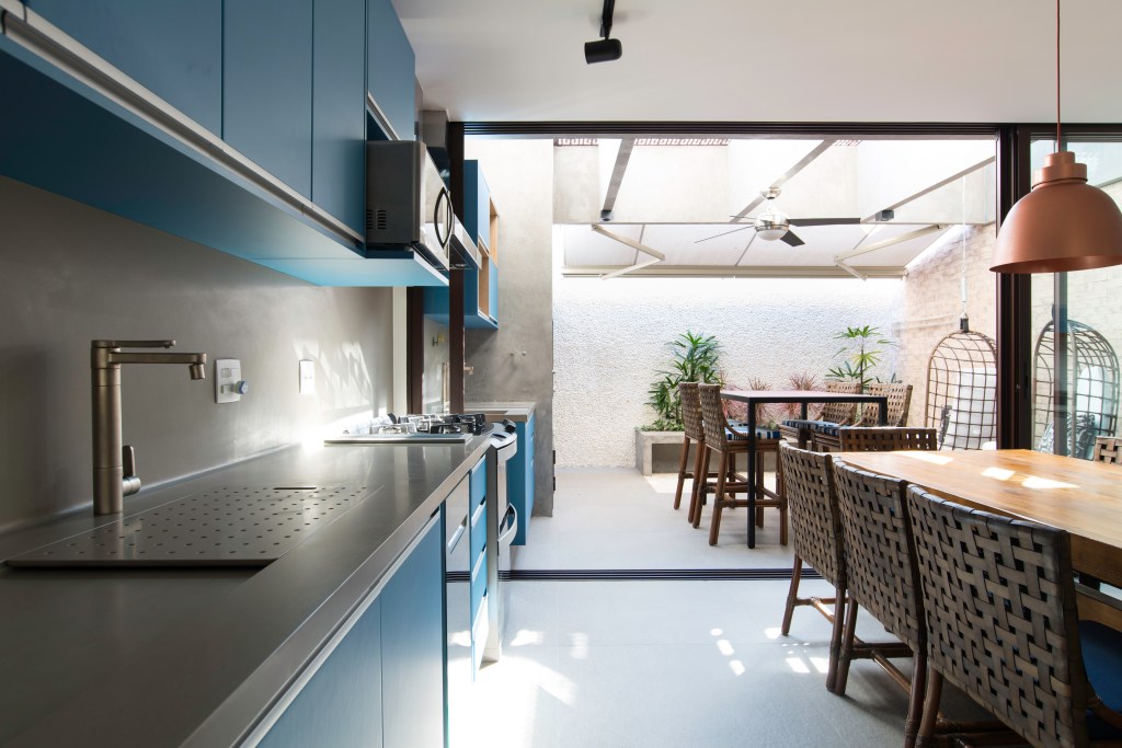 Cozinha com copa integrada com área externa; bancada de Corian e marcenaria azul.