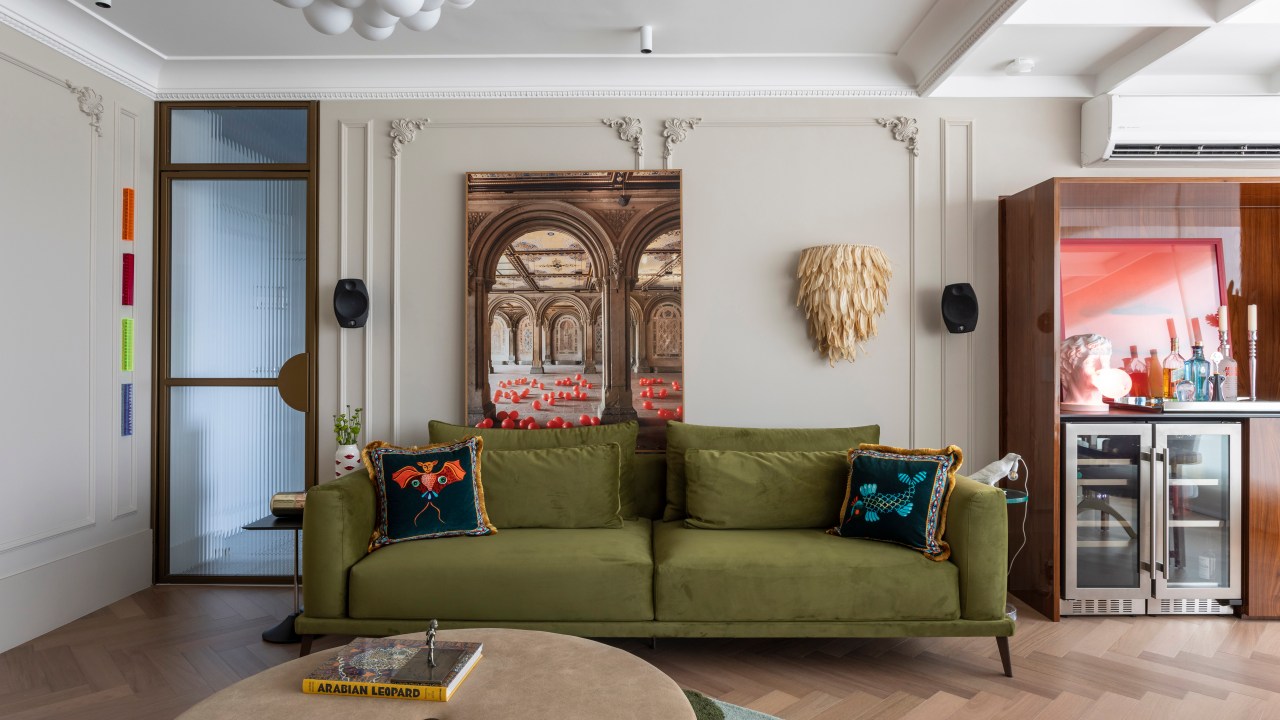 Sala de estar com boiseries, luminária, sofá verde, cristaleira e tapete colorido.