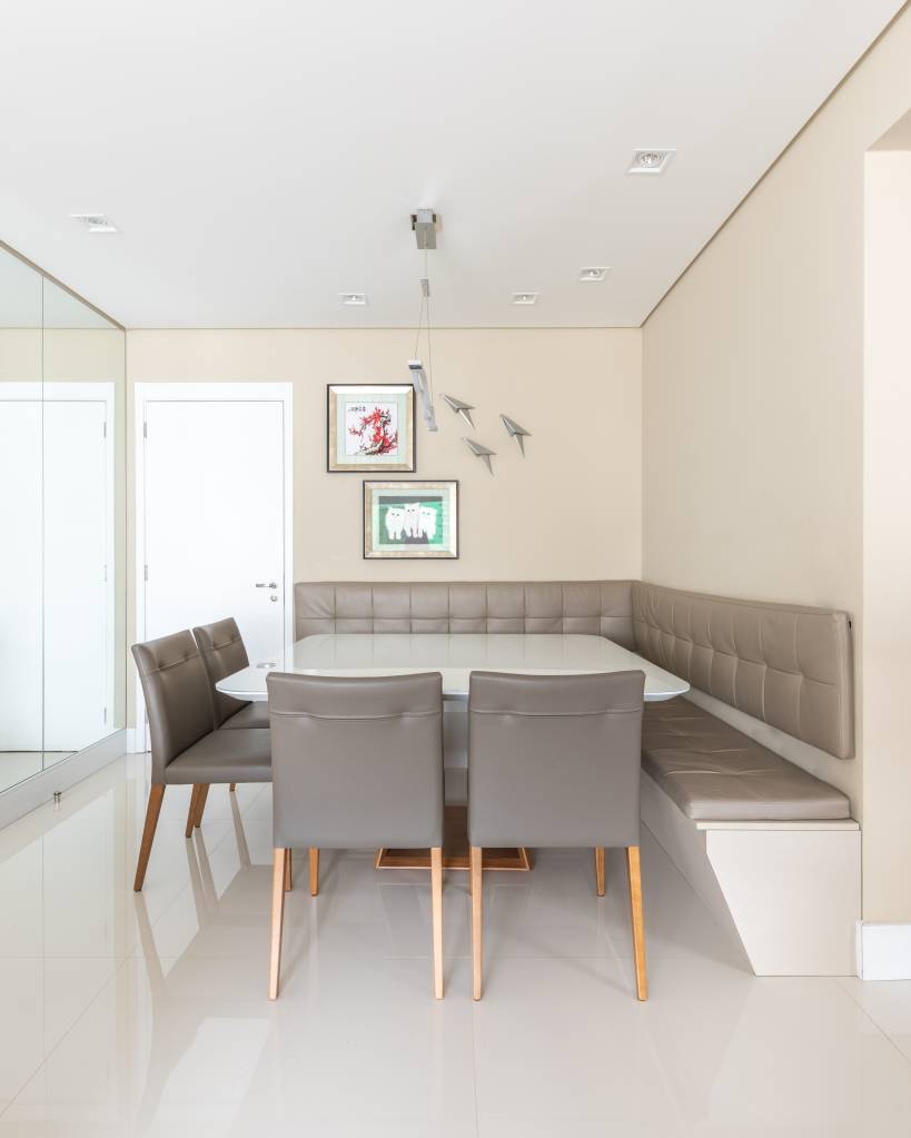 Sala de jantar com piso de porcelanato laqueado, mesa branca e canto alemão com assento cinza.