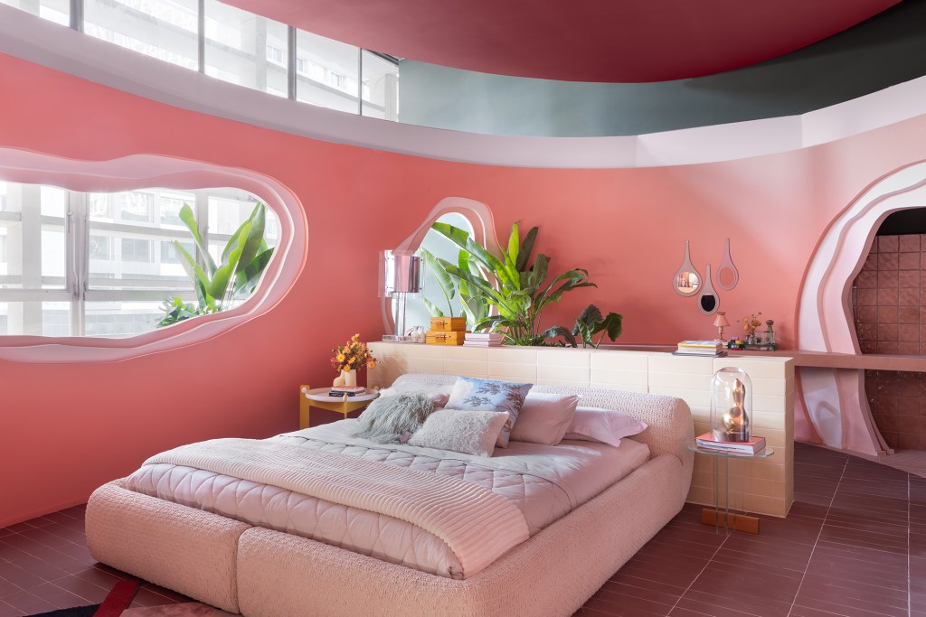 Casa rosa de 225 m² com cara de brinquedo feita para moradora de 64 anos. Projeto de Ricardo Abreu para a CASACOR SP 2023. Na foto, quarto com cama estofada, tapete geométrico e paredes rosas.