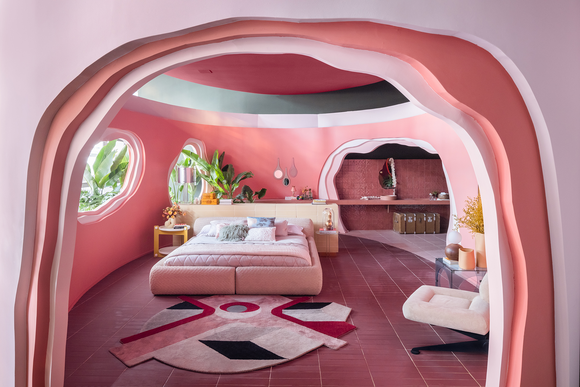 Casa rosa de 225 m² com cara de brinquedo feita para moradora de 64 anos. Projeto de Ricardo Abreu para a CASACOR SP 2023. Na foto, quarto com cama estofada, tapete geométrico e paredes rosas.