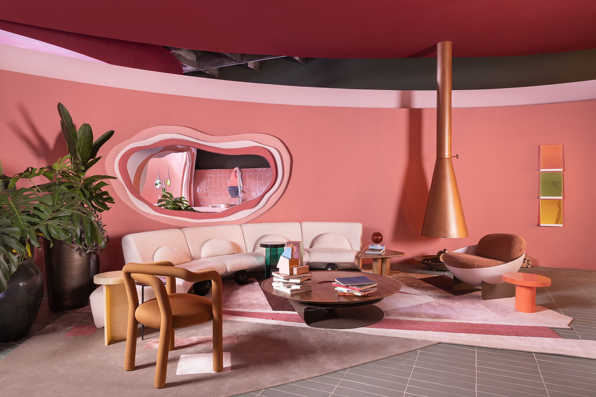 Casa rosa de 225 m² com cara de brinquedo feita para moradora de 64 anos. Projeto de Ricardo Abreu para a CASACOR SP 2023. Na foto, sala de estar com parede rosa, lareira e sofá curvo.
