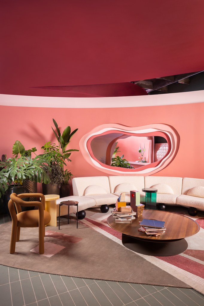 Casa rosa de 225 m² com cara de brinquedo feita para moradora de 64 anos. Projeto de Ricardo Abreu para a CASACOR SP 2023. Na foto, sala de estar com parede rosa, vasos e sofá curvo.
