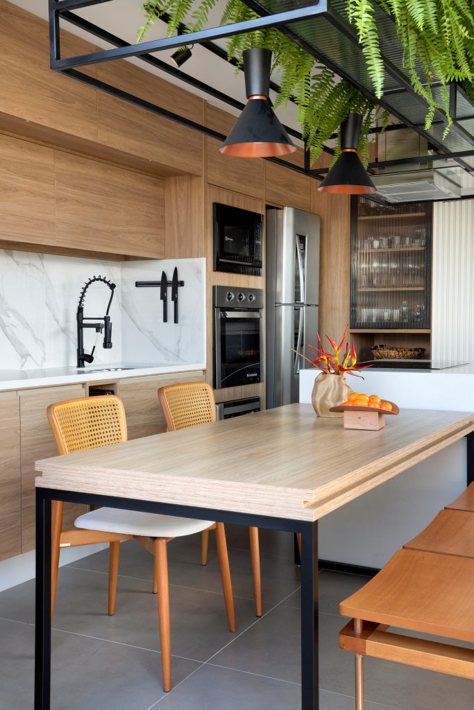 Cozinha gourmet integrada com mesa de madeira, bancada branca, marcenaria com backsplash marmorizado.