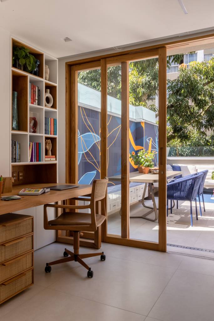 Home office com vista para terraço, bancada de madeira e estante de nichos.