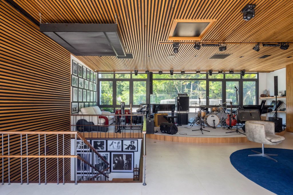 Cobertura triplex possui entrada privativa da rua e estúdio de música. Projeto de Mauricio Nobrega. Na foto, sala de música com paredes e teto ripados, poltronas e vista para a natureza.