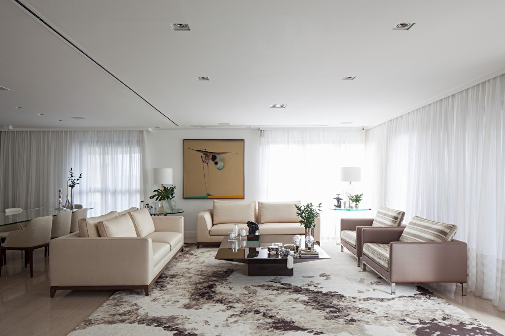 Sala de estar com tapete claro com estampas marrons e sofás claros.