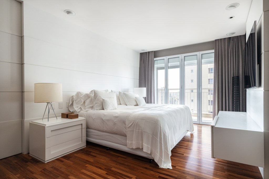 Quarto minimalista com piso de madeira, cama de casal, mesa lateral e piso de madeira.