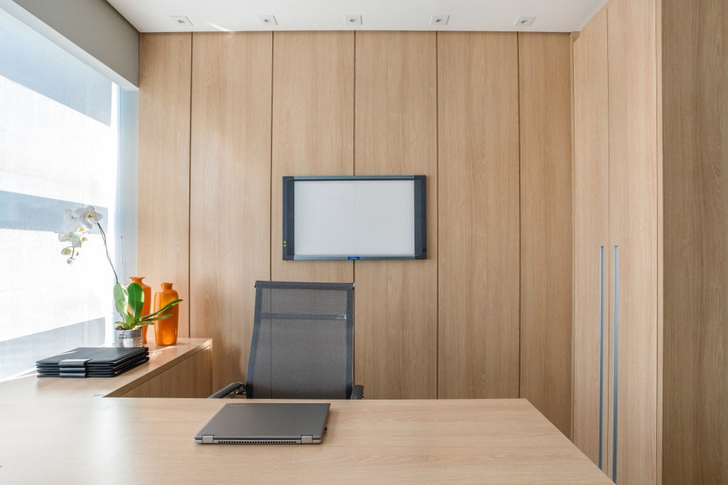 Home office minimalista com mesa de madeira e paredes revestidas de madeira.