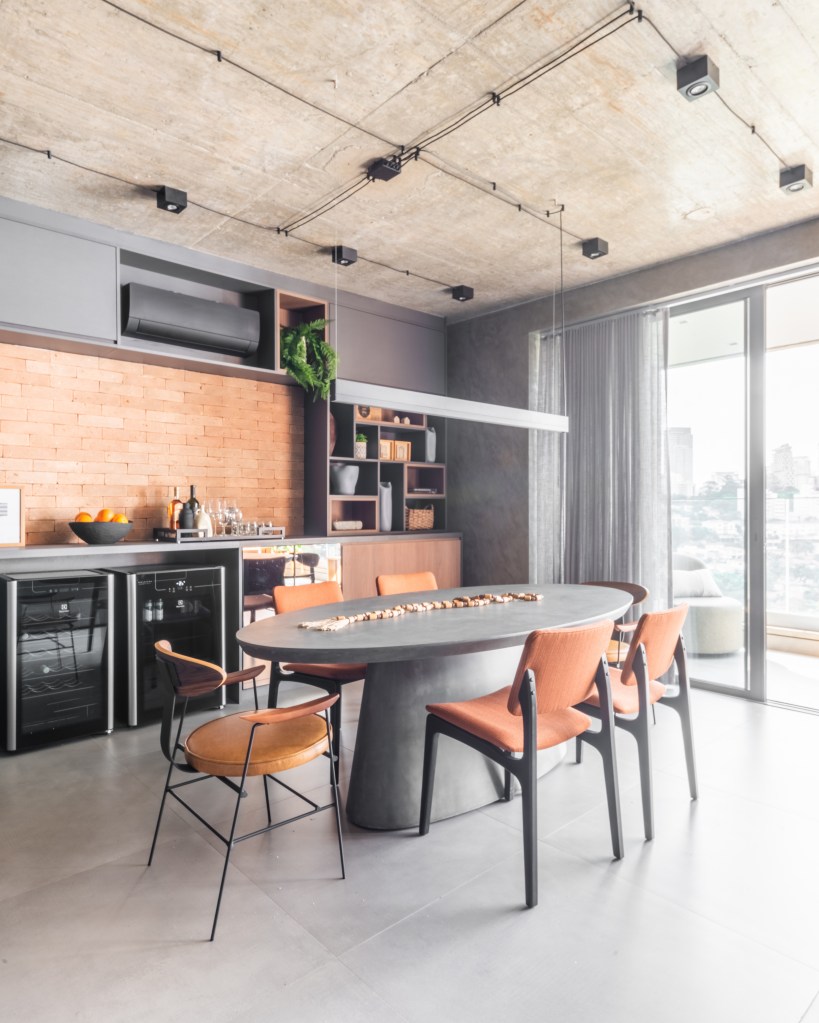 Cozinha com piso de porcelanato, mesa oval cinza e marcenaria cinza.