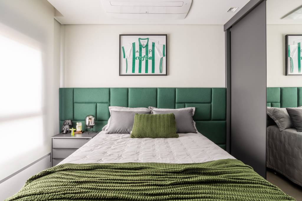 Quarto com travesseiros e marcenaria cinza, com cabeceira acolchoada verde.