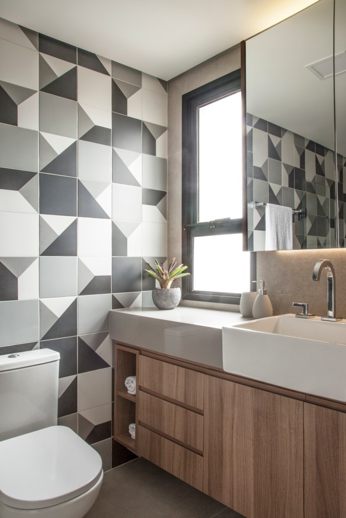 Banheiro com parede de azulejos geométricos cinzas.
