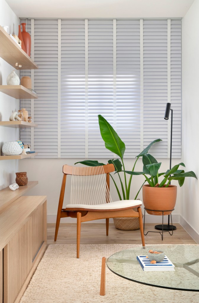 Sala; cantinho de leitura com cadeira de madeira, plantas e persiana.
