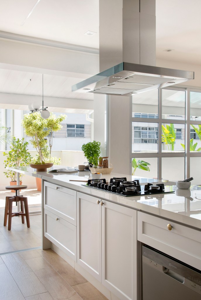 Cozinha branca clássica integrada com marcenaria branca, ilha com cooktop.