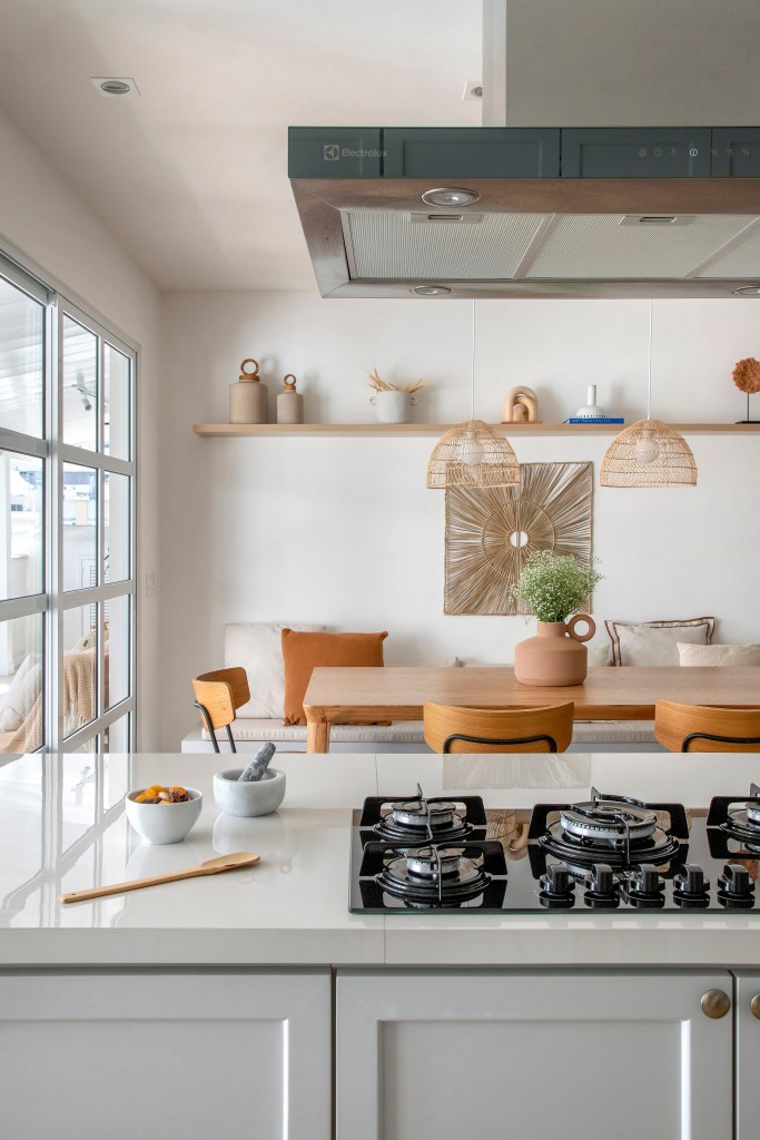Cozinha integrada; bancada branca com cooktop e sala de jantar com mesa de madeira.