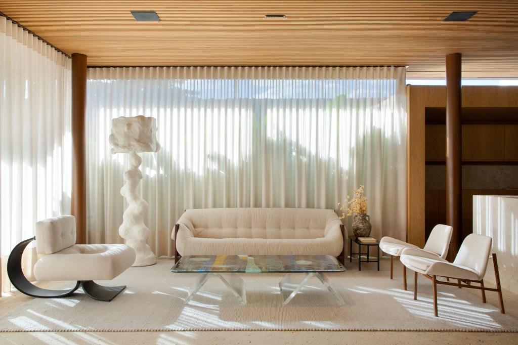 Escritório de 160 m² tem cara de casa de campo e bar na recepção. Projeto Otto Felix. Na foto, living com parede de vidro, tapete, sofá branco e cortinas.
