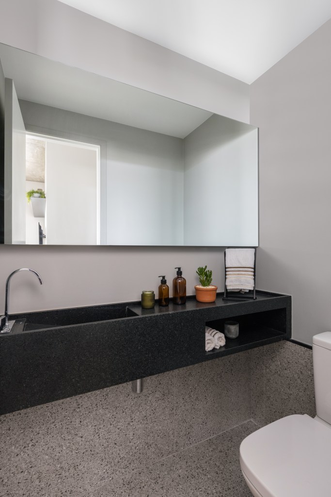 Banheiro com cuba esculpida e bancada preta, espelho grande.