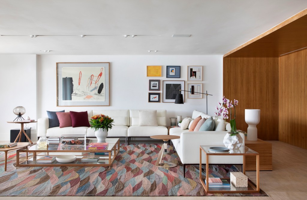 Sala de estar com tapete colorido, sofá branco grande, poltrona mole e quadros.
