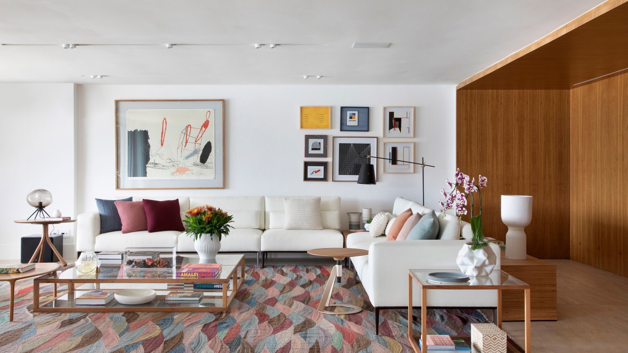 Sala de estar com tapete colorido, sofá branco grande, poltrona mole e quadros.