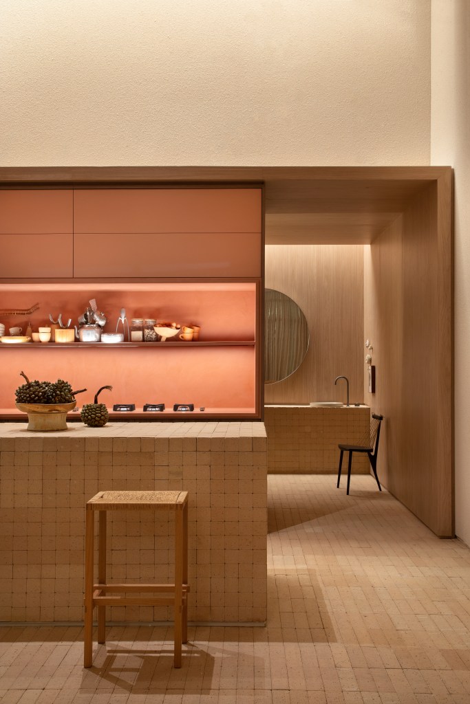 Loft de 120 m² é inspirado no caramujo aruá-do-mato. Projeto de Très Arquitetura para a CASACOR SP 2023. na foto, cozinha com ilha revestida de tijolinhos e armários rosas.