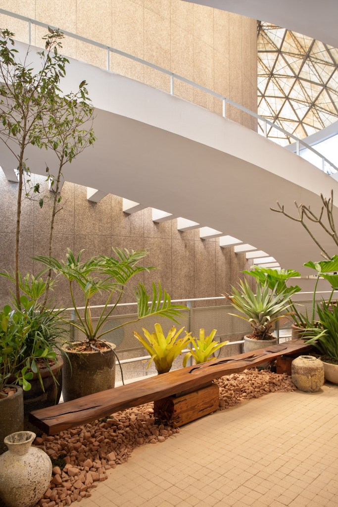 Loft de 120 m² é inspirado no caramujo aruá-do-mato. Projeto de Très Arquitetura para a CASACOR SP 2023. Na foto, jardim com banco de madeira e seixos.