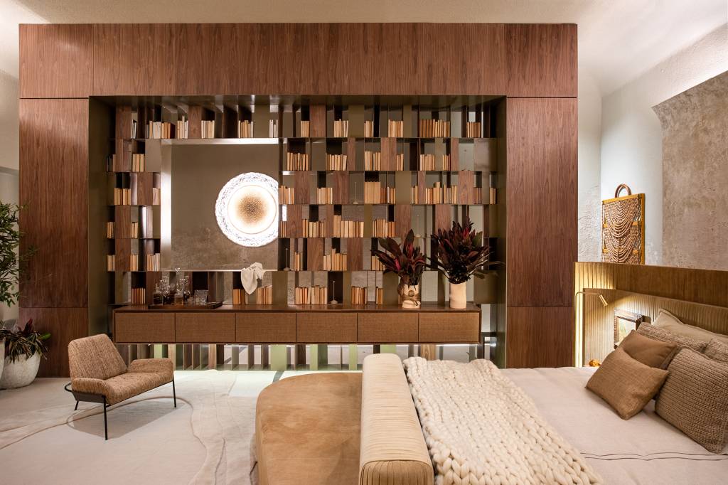 Marcas do tempo e histórias marcam o décor deste loft. Projeto de SUITE Arquitetos para a CASACOR SP 2023. Na foto, quarto com estante de marcenaria, cama estofada e pedras.