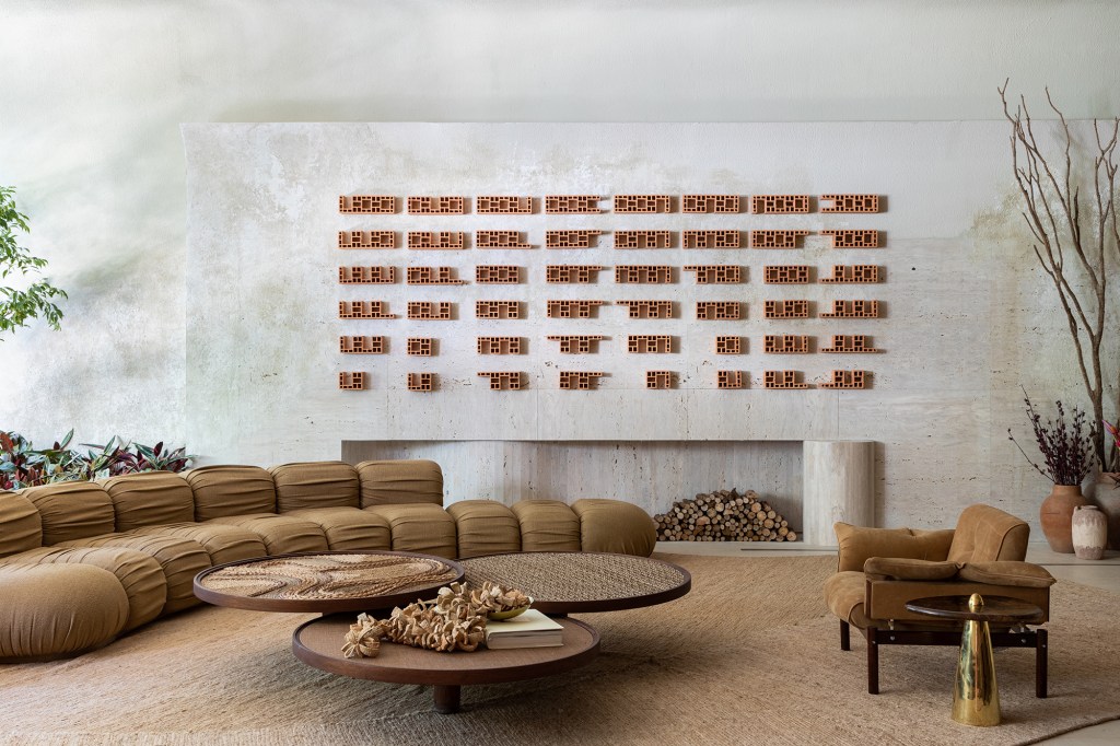 Marcas do tempo e histórias marcam o décor deste loft. Projeto de SUITE Arquitetos para a CASACOR SP 2023. Na foto, sala com tijolos na parede, sofá curvo e mesas.