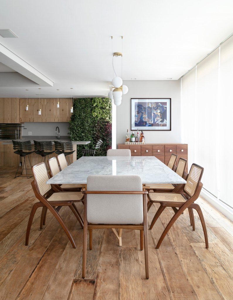 Sala de jantar em varanda integrada com mesa de tampo marmorizado branco e cadeiras de madeira.