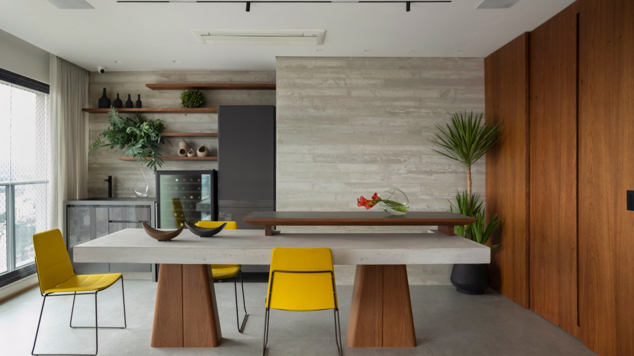 Área gourmet com mesa de concreto, cadeiras amarelas, marcenaria laqueada cinza e adega.