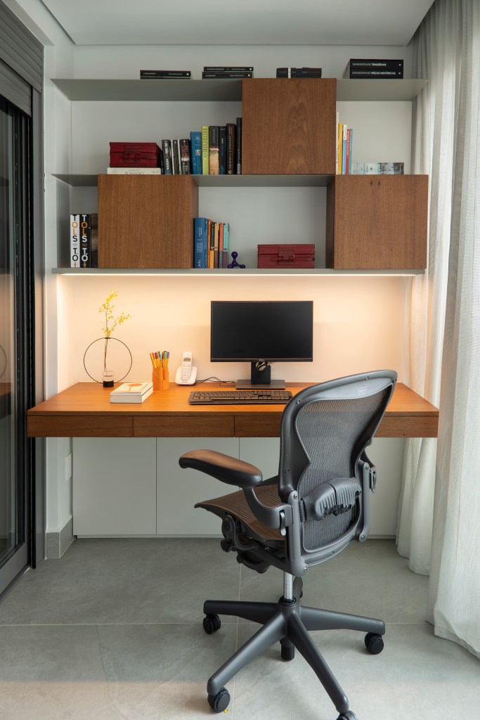 Home office com mesa de madeira, cadeira de escritório, estante com nichos.