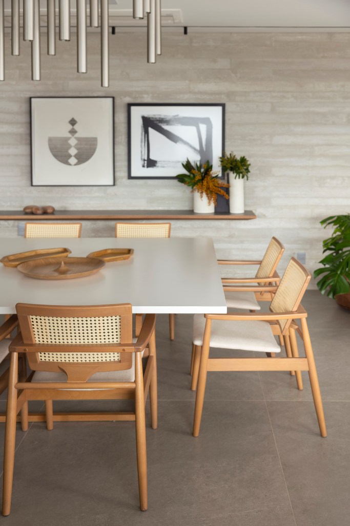 Sala de jantar com mesa com tampo branco laqueada, luminária e cadeiras de madeira com palhinha.
