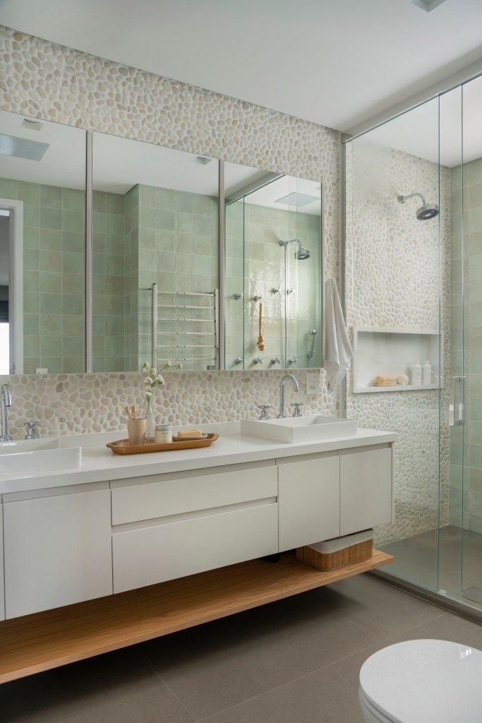 Banheiro com ladrilhos, marcenaria branca e armário aéreo espelhado.