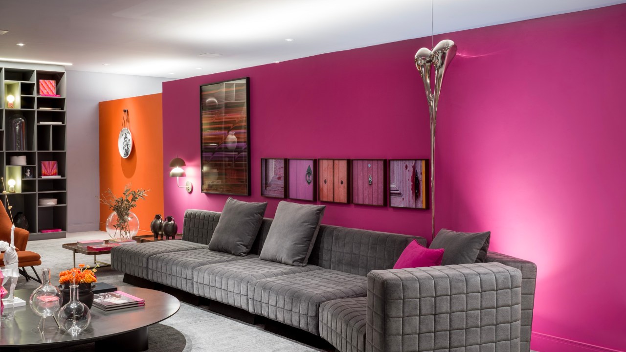 Sala com sofá de veludo cinza, tapete cinza e parede rosa.