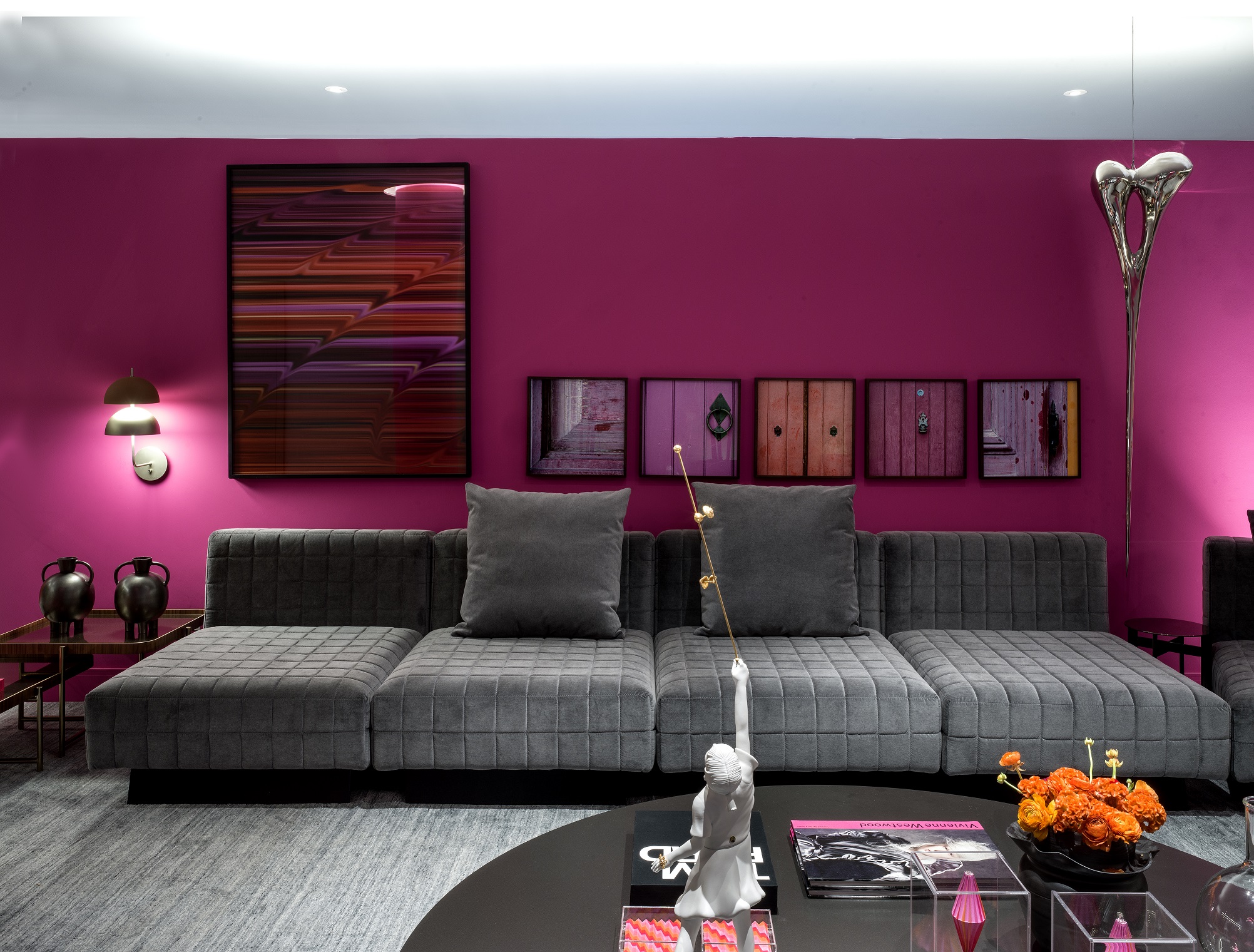Sala com sofá de veludo cinza, tapete cinza e parede rosa.
