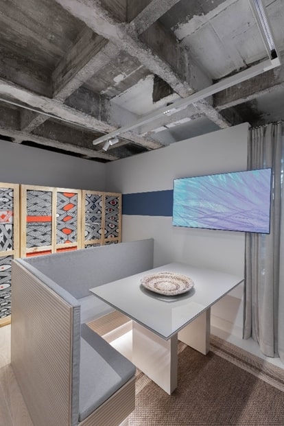 Sala de jantar com mesa e banco cinza, armário com grafismos.