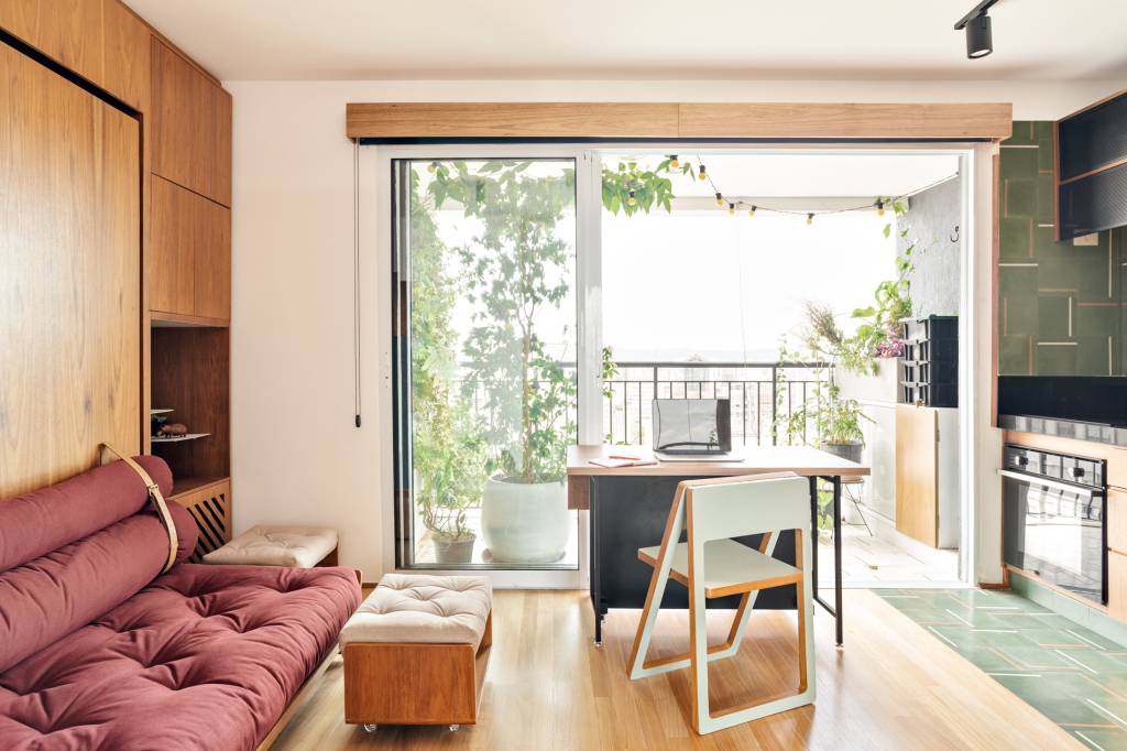 Sala de estar com piso de madeira, sofá vermelho, mesa pequena de home office.