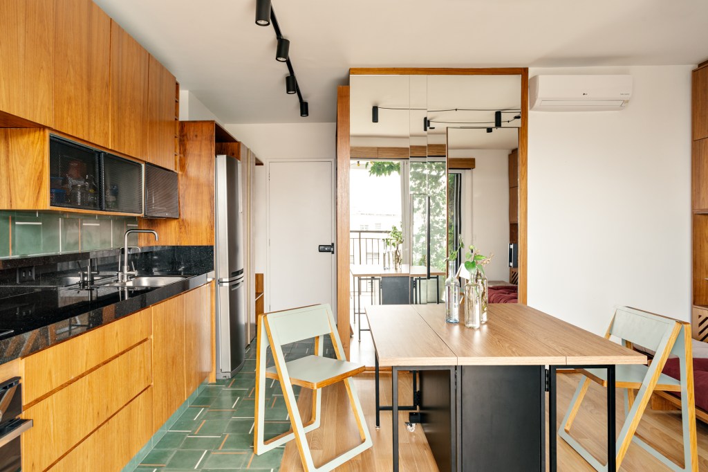 Cozinha integrada com sala de estar com mesa de madeira, piso de ladrilho hidráulico verde, espelho.