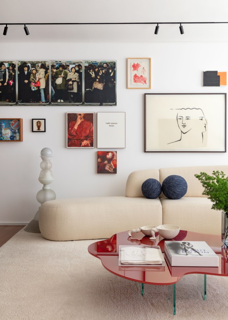 Sala de estar com tapete off white, sofá curvo, mesa de centro vermelha e quadros atrás do sofá.