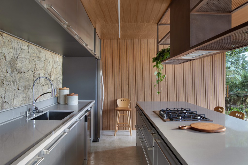 Cozinha integrada com marcenaria cinza e parede com ripas de madeira.